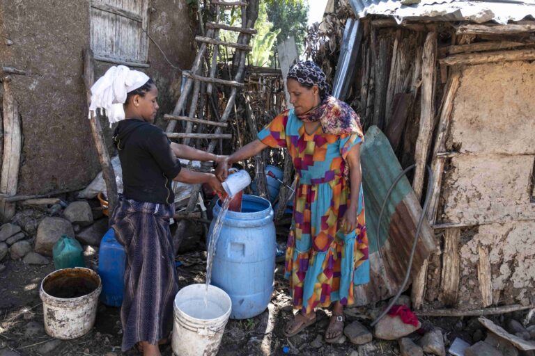 Mutter und Tochter schöpfen Wasser aus ihrer Wassertonne